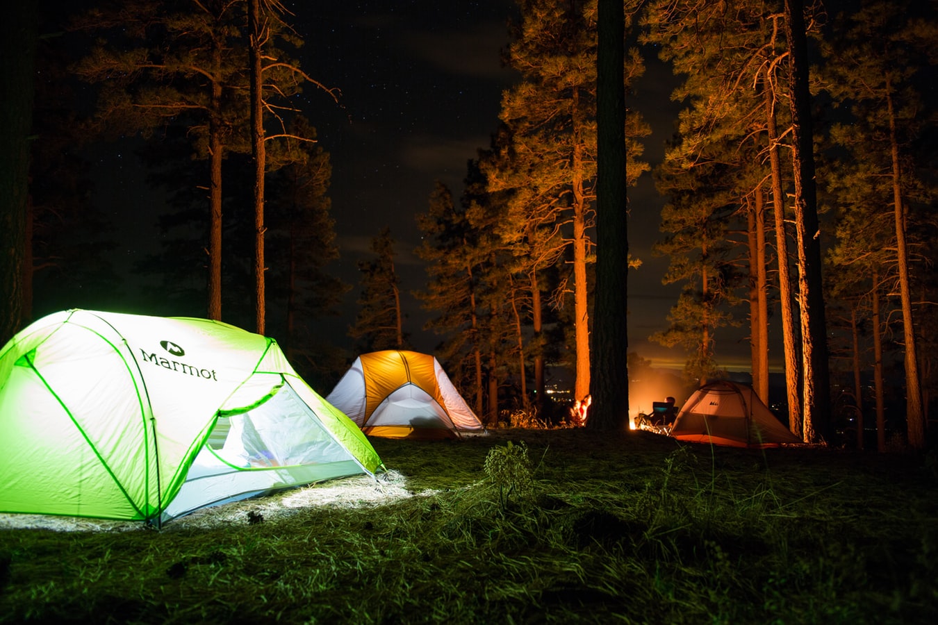 Three tents illuminated in the darkness by lamps and campfire