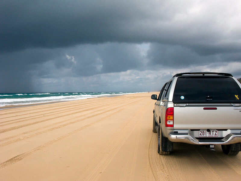 Silver 4wd driving across the beach as a storm rolls in